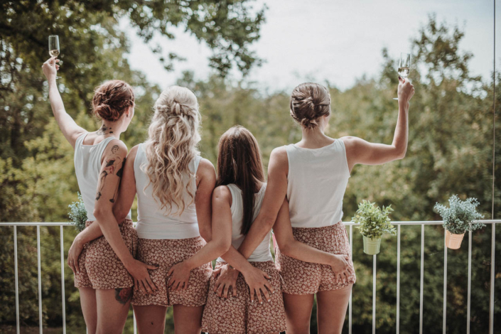 Braut mit Trauzeuginnen im selben Look auf dem Balkon mit Sekt in der Hand