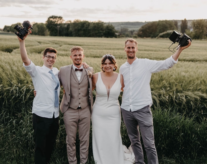 Hochzeitsfilmer mit Brautpaar vor Feld